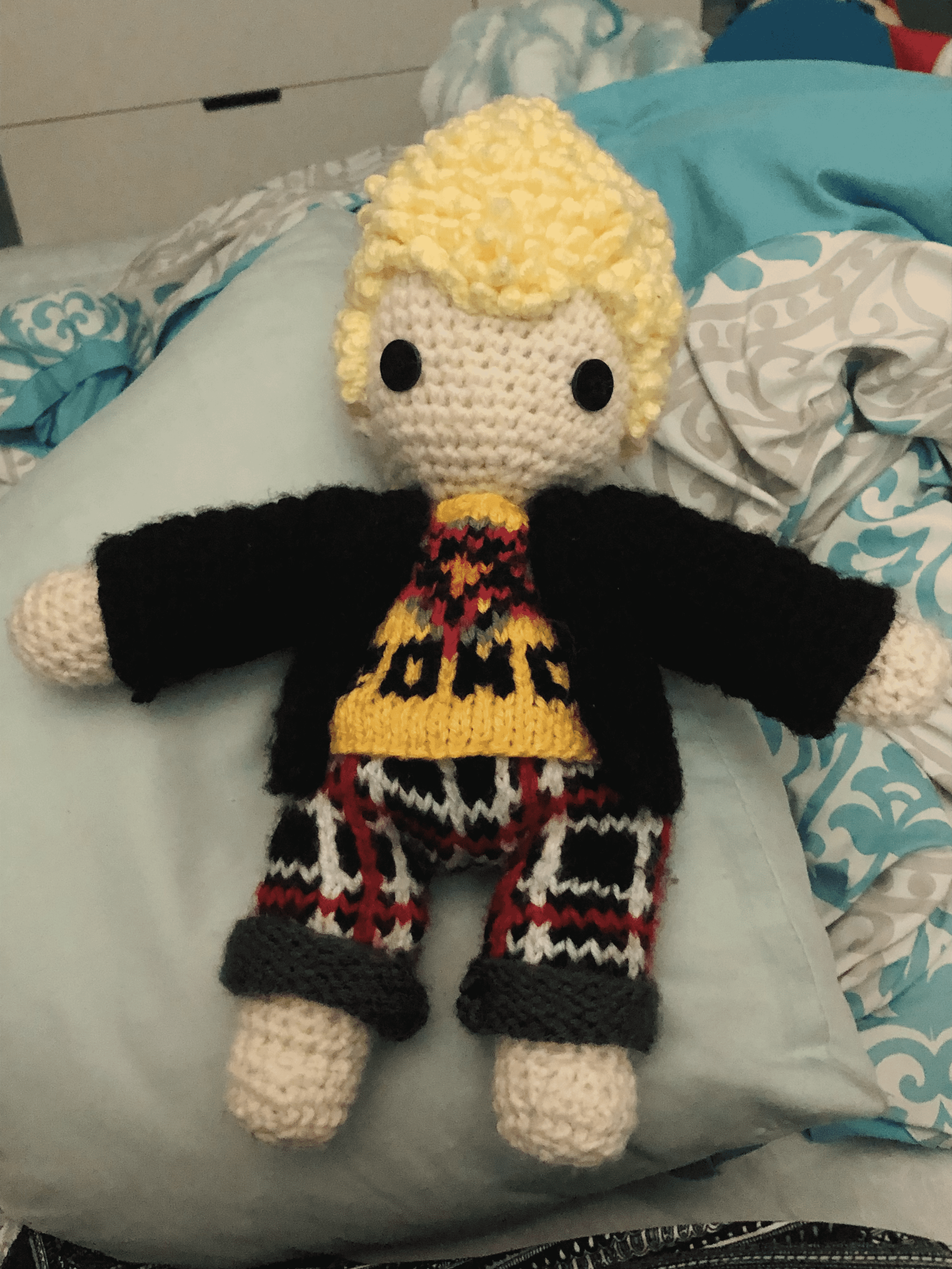 An amigurumi crocheted doll with blonde hair and knit and crocheted clothes